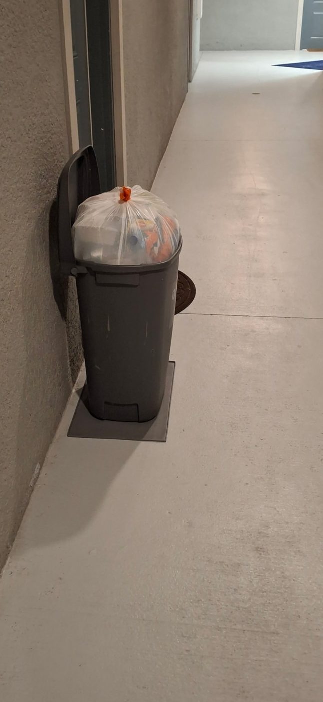 Tied trash bag in a bin by an apartment door