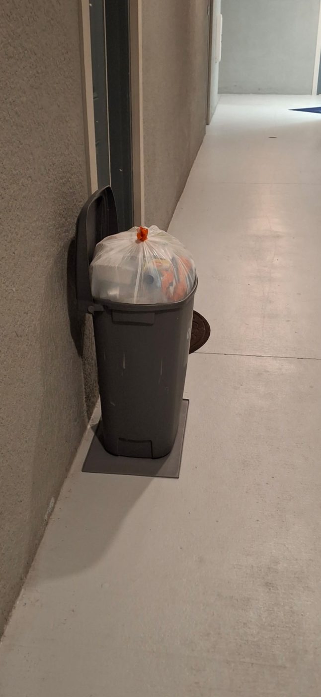 Tied trash bag in a bin by an apartment door