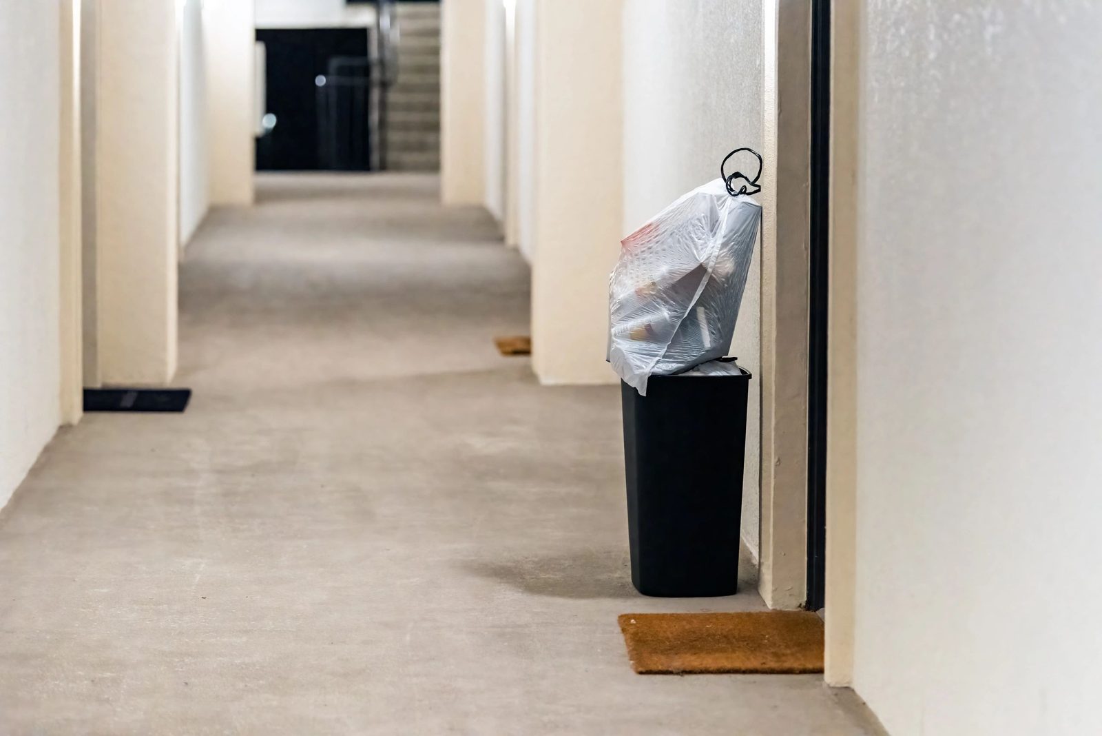 Tied trash bag in a bin in an apartment hallway